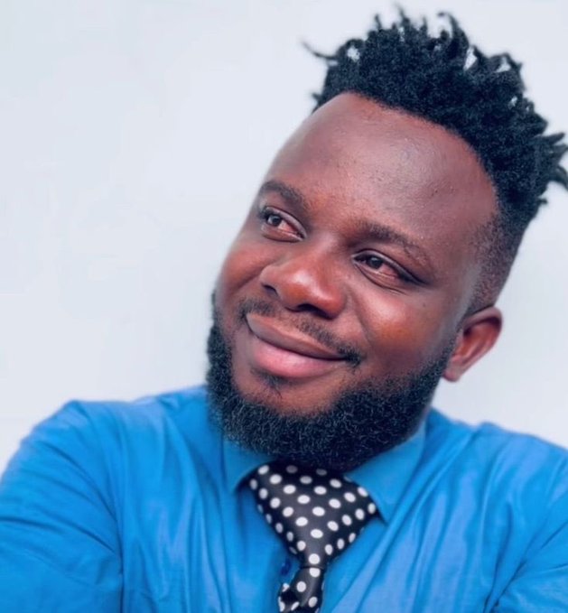 Portrait of a smiling Black man with a short beard wearing a blue shirt and a black polka-dot tie.