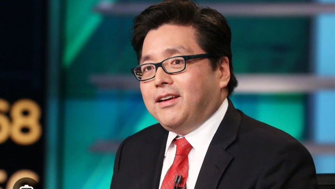 A man wearing black-rimmed glasses, a dark suit, white shirt, and red tie speaks in what appears to be a television studio setting.