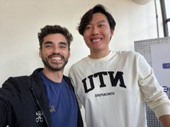 The image features two men standing next to each other, both smiling at the camera. One of them has a beard and appears to be Asian, while the other man is wearing a white sweatshirt with black text that says "UTN". They are positioned in front of a wall, which serves as their backdrop for this photo session. The image also contains some text that reads "$Zbase integrate into $bankr/ @base APAC ute base finalist Young handsome Chinese man @goheesheng you have everything going for you even an Elite based @bankrbot community".
