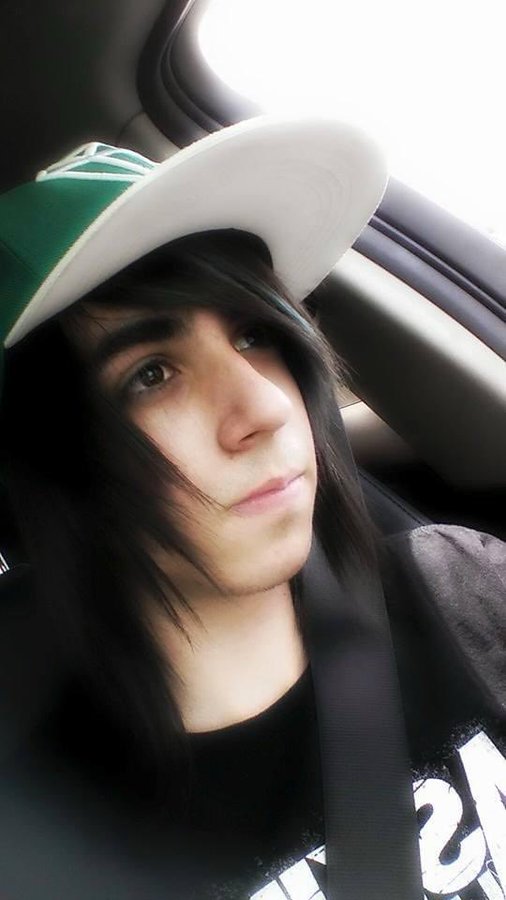 A person with long dark hair wearing a green and white cap taking a selfie while sitting in a car with a seatbelt on.