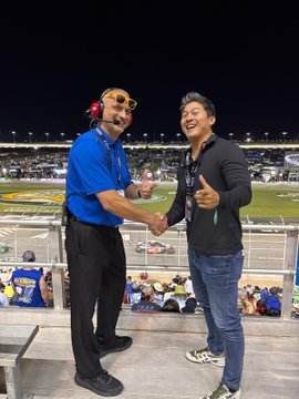 Two men shake hands and smile at a NASCAR race under stadium lights, with the crowd and track visible behind them, fitting the post's tone of playful hype around $WEN's NASCAR partnership and "global domination."