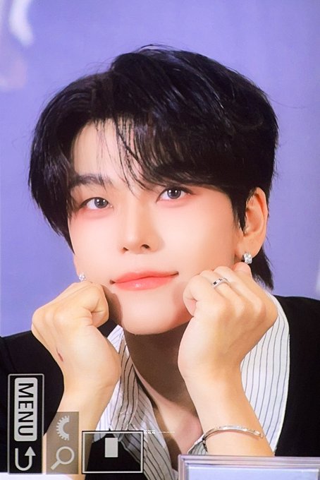 A young man with dark hair, wearing a striped shirt and silver jewelry, rests his chin on his hands with a gentle smile against a soft purple background. The image appears to be a photo card featuring Xinlong from Alpha Drive One, as indicated by the hashtags in the post.