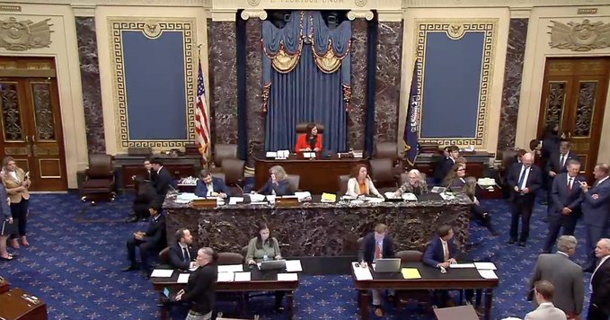The image shows the U.S. Senate chamber during a formal session, with senators and staff gathered around desks while the presiding officer sits at the elevated dais beneath the gold-fringed canopy. The caption "satoshi died for this" appears to be a sarcastic commentary criticizing what the poster views as excessive government regulation or bureaucratic oversight, suggesting that Satoshi Nakamoto's vision of decentralized cryptocurrency has been undermined by traditional governmental proceedings.
