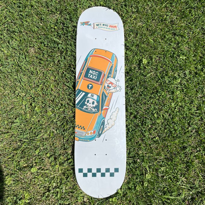 A skateboard deck with 'NFT NYC 2026' branding and cartoon artwork of an orange NYC taxi with a character driving lies on green grass.