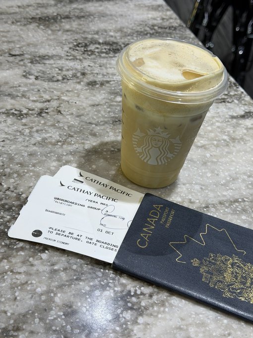 An iced Starbucks coffee sits on a speckled countertop next to a Cathay Pacific boarding pass for flight CX829 (Hong Kong to Vancouver) departing October 1st, and a Canadian passport—perfect travel companions marking the beginning of a 25-hour journey.