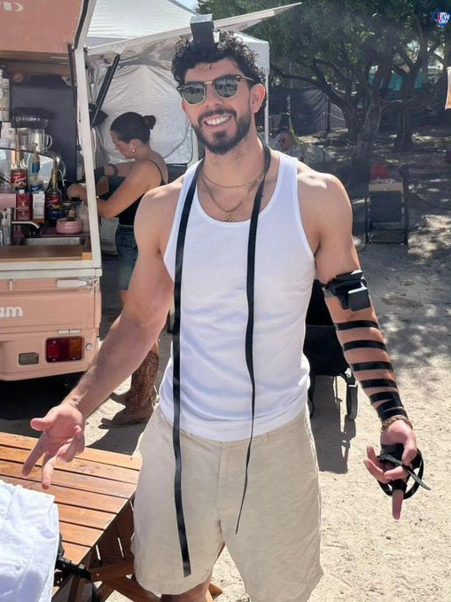 A bearded man in a white tank top and sunglasses smiles cheerfully in front of a pink food truck, with another person working inside. The caption's mention of feeling happier than in weeks alongside crypto tickers $SOL and $BTC suggests the upbeat pose may reflect a positive mood tied to those assets.