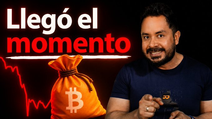 The image features a man sitting next to an orange bag, which has the word "bitcoin" written on it. The man appears to be smiling at the camera while holding up his hand. In the background of the image, there are two lines drawn in red and white colors that say "LEGO EL MOMENTO".