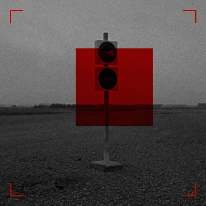 A grainy, monochrome image of a traffic signal with a red overlay box covering it, set in an empty landscape with red corner brackets framing the scene.