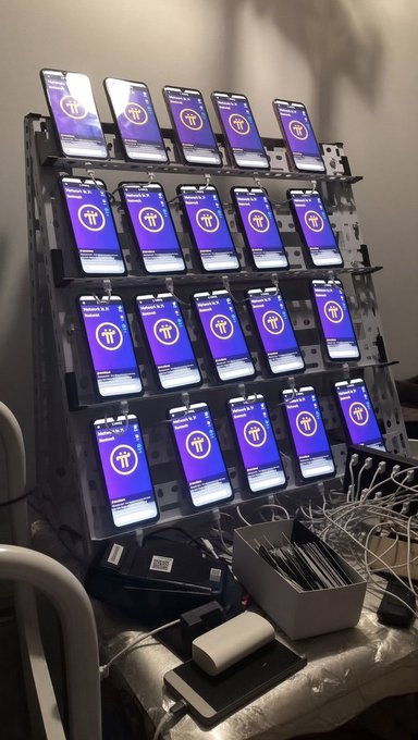 Multiple smartphones are mounted on a rack, each running a Pi Network (PI) KYC verification interface, with cables visible for simultaneous operation—reflecting the post's message about setting up many accounts to maximize potential airdrop rewards.