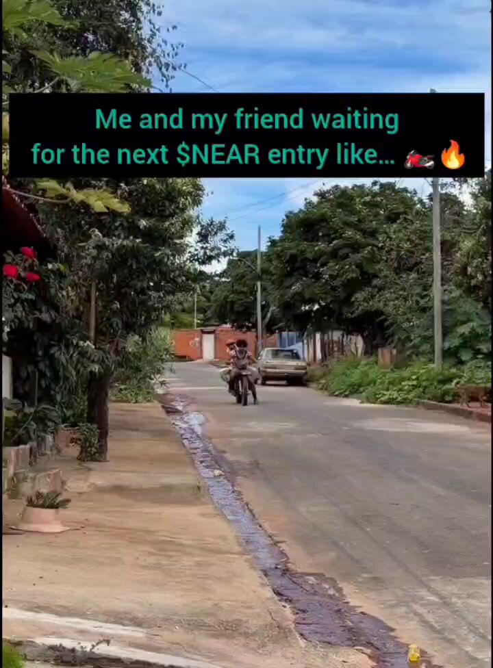 The image shows a person riding a motorcycle down a street, with a car following behind them. The motorcyclist appears to be driving away from the camera. In the background, there are trees lining the street, adding to the urban setting of the scene. The caption for this image is "Me and my friend waiting for the next snear entry like."
