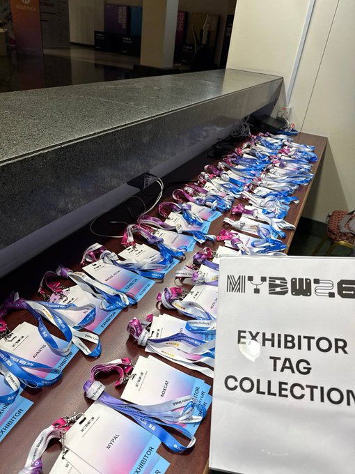 A photo of numerous exhibitor badges and lanyards laid out on a table at what appears to be a trade show, next to a sign reading 'EXHIBITOR TAG COLLECTION'.