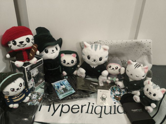 A collection of cat-themed crocheted dolls and merchandise arranged on a table with a 'hyperliquid' branded mat.