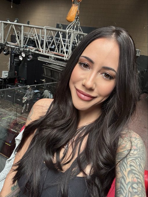 A smiling woman with long dark hair poses for a selfie in front of a concert stage with scaffolding and equipment visible in the background, while her post celebrates $ZEC hitting an all-time high and $BTC returning to $85,000 on a good morning.
