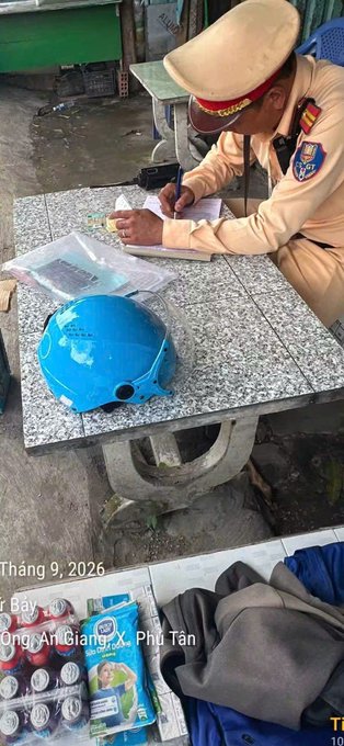 A traffic police officer in uniform writes on a notepad at a stone table, with a blue helmet and evidence bags visible.