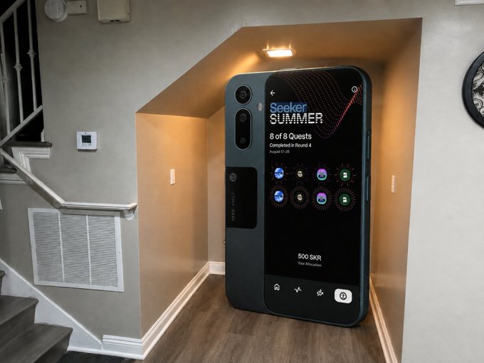 A giant smartphone displaying a "Seeker Summer" quest completion screen showing "8 of 8 Guests Completed in Round 4" and "500 SKR" allocation stands in a hallway under a staircase, suggesting an oversized screen would be a striking installation piece for the space.