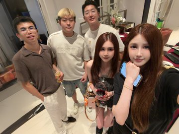 A group selfie of five young people indoors, including a woman holding a small dog wearing a sweater.