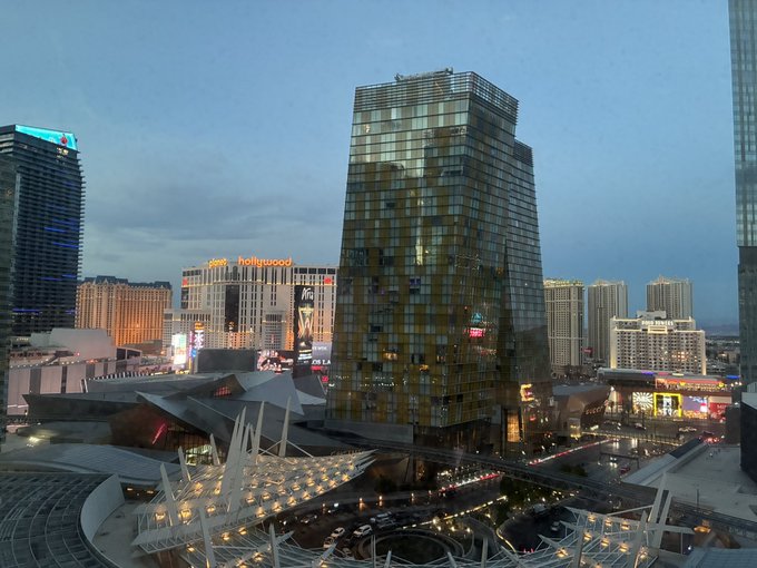 An evening cityscape view of the Las Vegas Strip featuring Planet Hollywood hotel and casino with its distinctive golden glass facade, alongside the Aria resort.