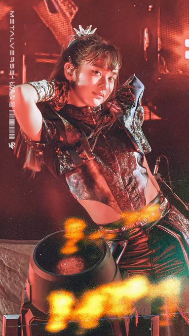 A concert photo shows a female performer with a small crown on her head, wearing an elaborate stage outfit and gloves, standing near a stage prop with flames.