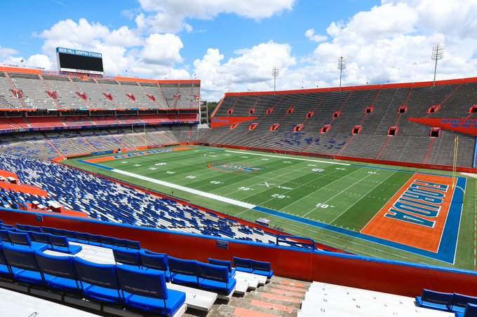 An empty Ben Hill Griffin Stadium (the Florida Gators' home field) is shown on a sunny day, with "FLORIDA" displayed in the end zone and the scoreboard reading "BEN HILL GRIFFIN STADIUM." The image ties to the post by showing the iconic Florida Gators football venue, where a retro Emmitt Smith jersey would be worn, playfully suggesting the addition of an XRP logo to it.