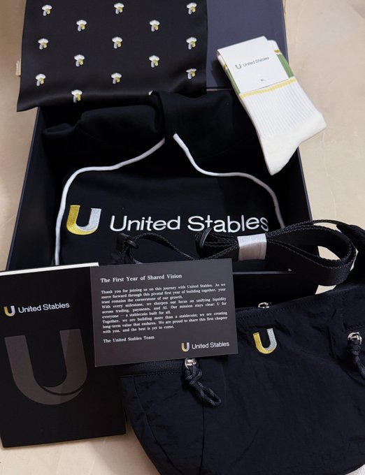 An open promotional box from 'United Stables' contains black merchandise including a bandana, socks, a drawstring pouch, and a card reading 'The First Year of Shared Vision'.