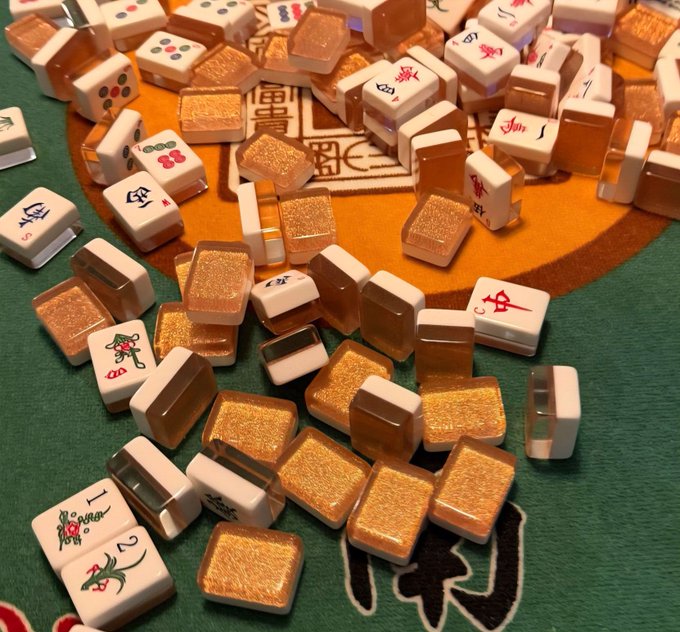 The image features a large pile of colorful jigsaw puzzle pieces scattered across a green surface. The puzzle pieces are made from glass and have various designs, including Chinese characters that read "大阪", which translates to "Chinese tiles". The scene suggests an interest in puzzles or games involving these unique pieces.