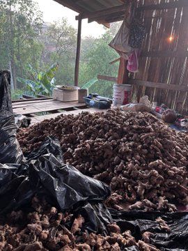 urns of food, including a large pile and smaller stacks, are scattered on the ground inside a rustic wooden structure with a thatched roof.