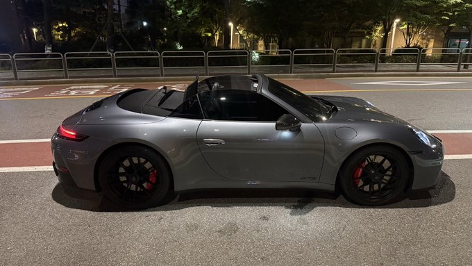 A gray Porsche 911 Carrera 4 GTS Cabriolet is parked at night with the top down, revealing its black interior and red brake calipers, with "GTS" badging visible on the side. The caption reads, "My cousin suddenly hits me up like, 'Come on out, let's go for a drive!' The car he pulls up in is, Porsche 911 Carrera 4 GTS Cabriolet. Price tag: 300 million. Took it for a spin on Jayuro and I'm like 'This thing's killer.' Got the full internal combustion engine."