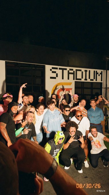 A group photo of people posing in front of a building with "STADIUM" written on it, dated 08/30/26, captured in a Meta AI format.