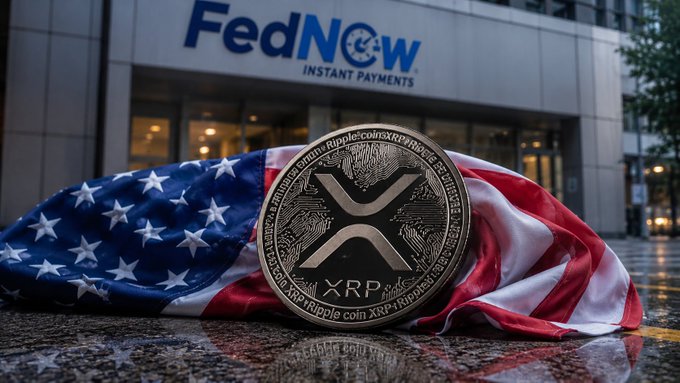 A physical XRP cryptocurrency coin resting on an American flag in front of a 'FedNow INSTANT PAYMENTS' building.