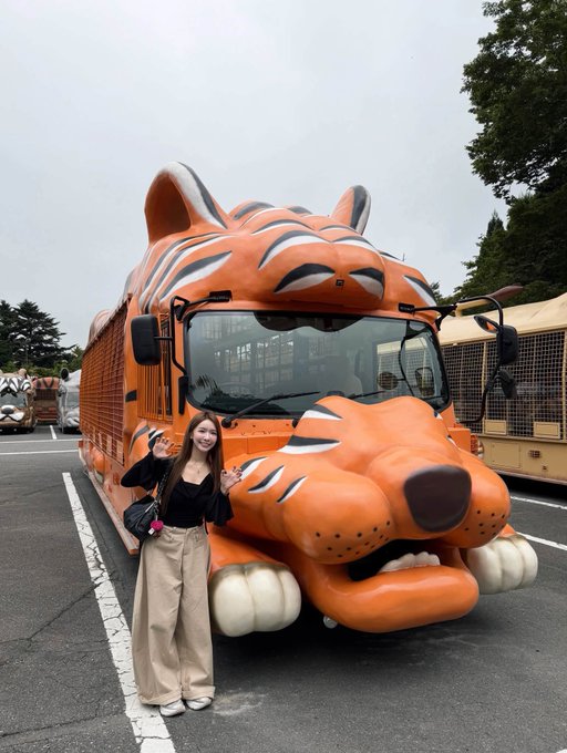 A young woman in a black top and beige pants stands smiling and posing next to a large orange tour bus shaped like a tiger.