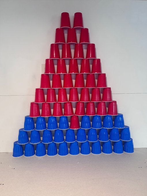 A pyramid structure built from stacked red and blue plastic cups against a white wall.