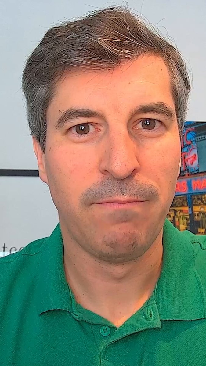 The image features a man wearing a green shirt with a mustache, looking directly at the camera. The background of the photo shows a white wall with a poster hanging on it that says "bitcopa has arrived: the OranjeBTC fanbase for Brazil in the Cup. During the World Cup, Brazil'S goals become BitGoool. For every goal by the Seleção, OranjeBTC will buy 1 whole Bitcoin for its treasury. And the fans join in too: the first 20 supporters who complete the steps". The man's facial expression and the poster behind him suggest that they are discussing or promoting a new product related to the World Cup.