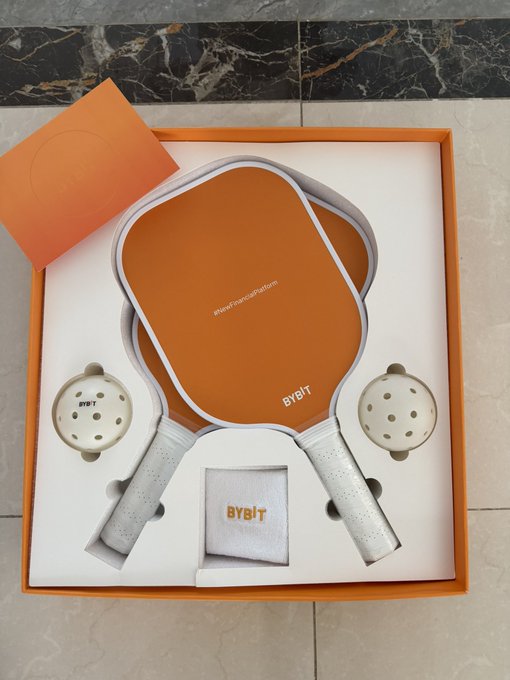Two orange BYBIT branded pickleball paddles and two balls are displayed in an orange presentation box.