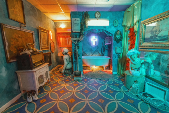 A photographic self-portrait of a surreal, immersive room bathed in moody teal and warm orange lighting, featuring a central clawfoot bathtub positioned in front of a glowing light box that substitutes for the absent photographer's reflection. The space is densely decorated with vintage oil paintings, classical busts, an ornate cabinet with a vintage radio, patterned tile flooring, and religious iconography like crosses, creating a haunting, theatrical atmosphere that evokes themes of solitude, surveillance, and existential reflection—reinforcing the post's caption "There Is No One Watching Out For Us." Visible text on a sign near the center reads "GENTLEMAN," and the accompanying social media text references the artwork's availability as an Ethereum-based NFT on OpenSea (opensea.io/item/ethereum/), aligning with the piece's digital art context.