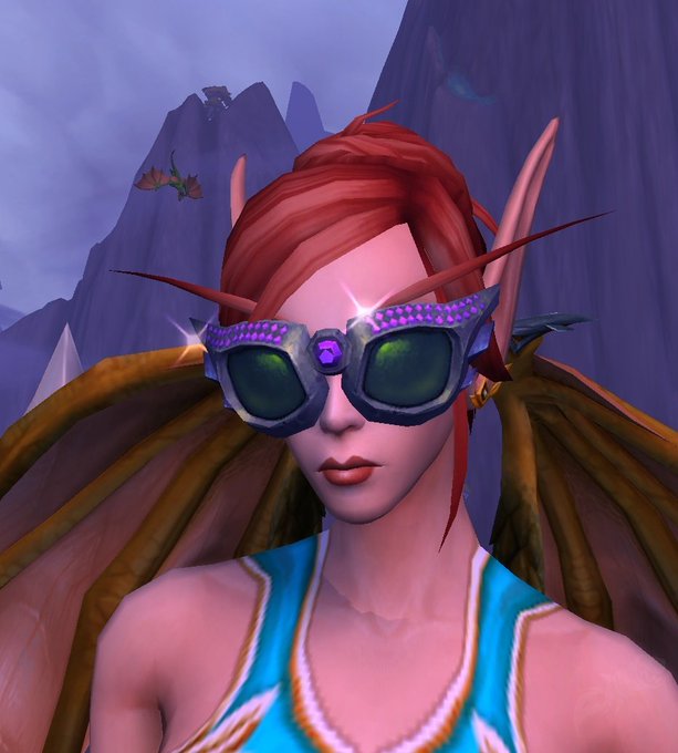 A World of Warcraft character portrait showing a blood elf female with red hair, pointed ears, purple gem-studded goggles, and a turquoise top against a mountainous background.