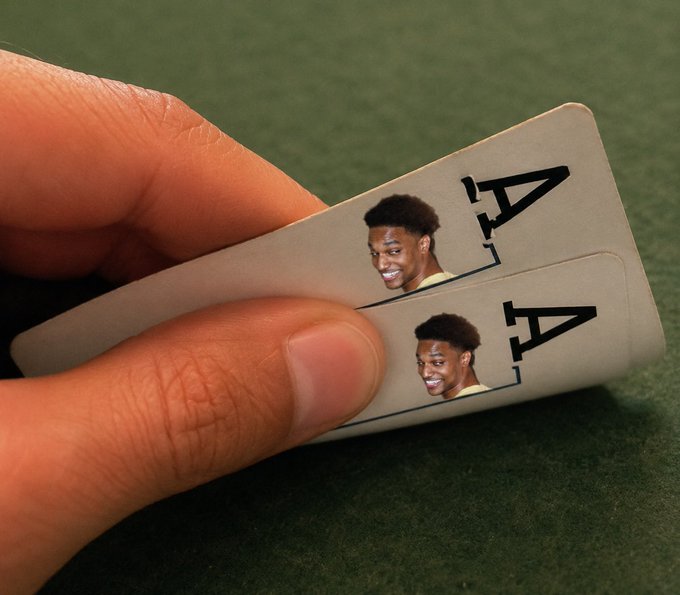 A hand holds two Ace of Spades playing cards that have been customized with a printed face of a smiling young basketball player on them.