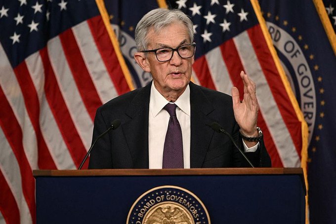 Federal Reserve Chair Jerome Powell speaks at a podium with the Board of Governors seal, flanked by American flags.
