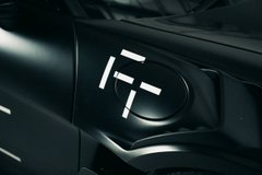 A close-up of a dark vehicle's front headlight displaying the illuminated 'FF' logo of Faraday Future.