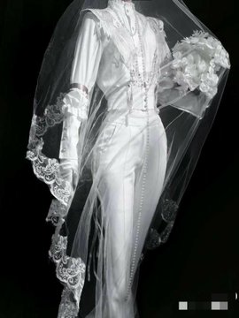 A white bridal gown and veil with lace detailing displayed on a mannequin against a dark background.