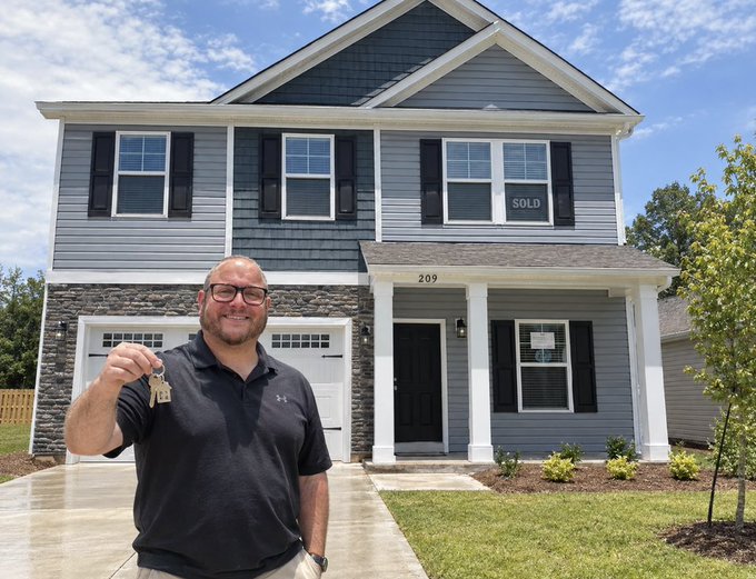 A man stands in front of a two-story blue house with a "SOLD" sign in the window, holding up keys and smiling, with the address "209" visible above the door.