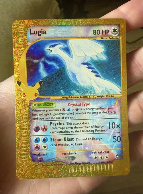 A hand holding a holographic gold Lugia Pokémon trading card showing 80 HP with 'Crystal Type' Poké-BODY, featuring 'Psychic' and 'Steam Blast' attacks.