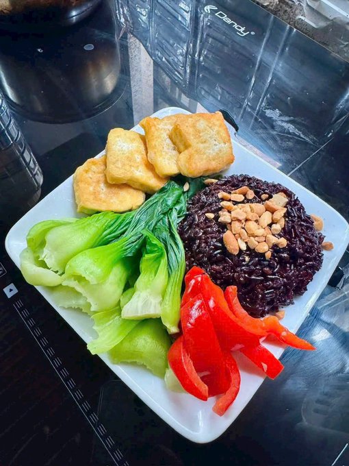 A plated meal featuring fried tofu, bok choy, red bell pepper slices, and a mound of purple black rice topped with crushed peanuts.