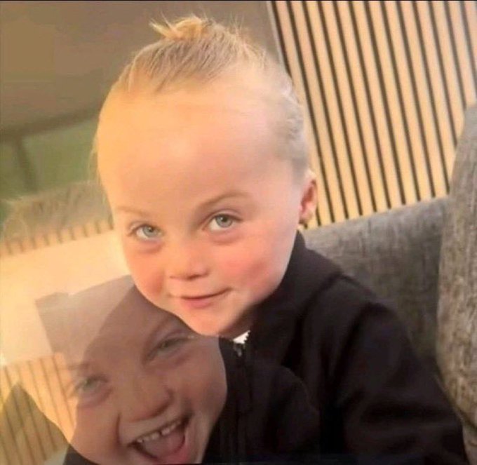 A close-up selfie of a smiling blonde child sitting on someone's shoulders.