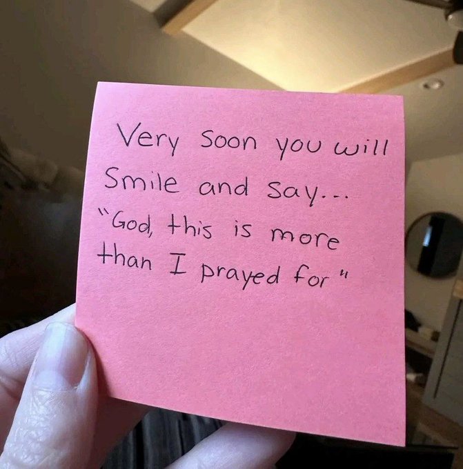 A hand holds a pink sticky note with handwritten text reading: 'Very soon you will smile and say... "God, this is more than I prayed for"'.