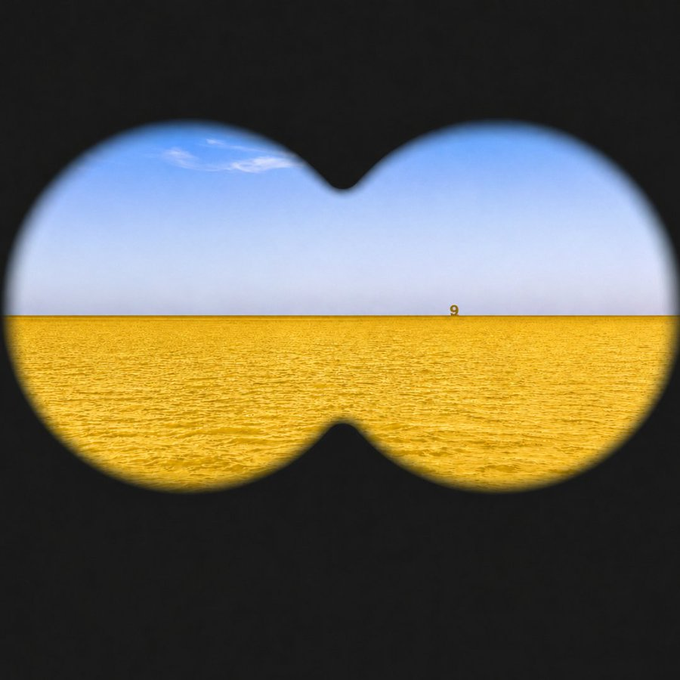 This image, viewed through binoculars, shows a solitary buoy with the number 9 on it in a vast yellow expanse under a blue sky, setting up the "Eye Test Challenge."