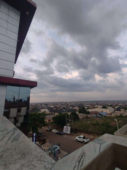 A landscape view from a high vantage point overlooking a town under a cloudy sky at dusk, with a building corner visible on the left.