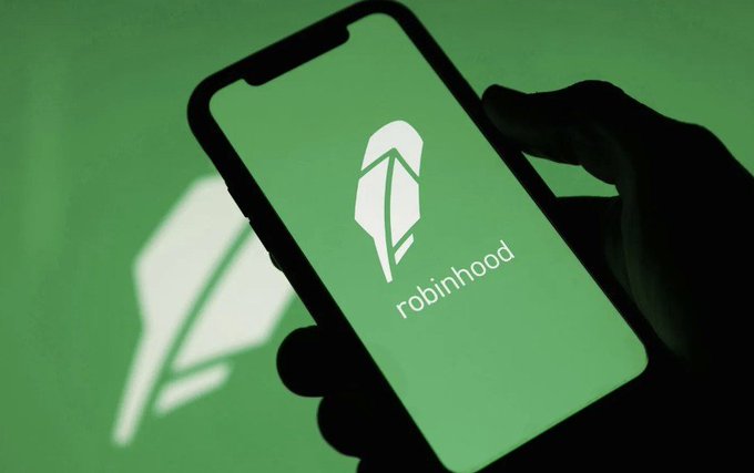 Silhouetted hand holding a smartphone displaying the Robinhood logo against a green background.