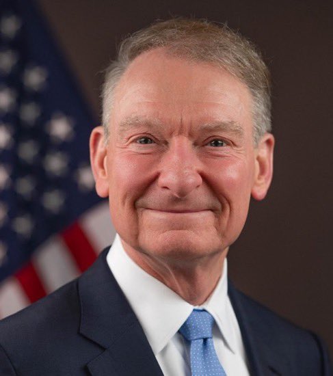 An official portrait of an older man in a dark suit and blue tie, smiling in front of an American flag, likely representing a SEC or financial regulatory official whose anticipated crypto-related announcement is the focus of the breaking story.