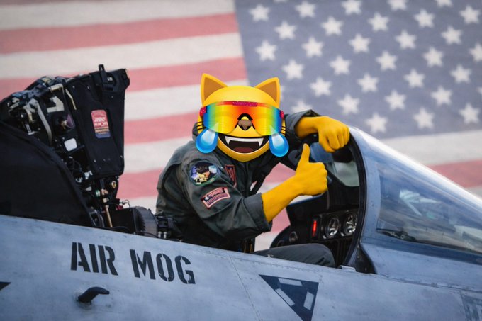 A pilot in a jet cockpit labeled "AIR MOG" gives a thumbs up, edited to have a crying-laughing yellow emoji face with rainbow sunglasses over the American flag.
