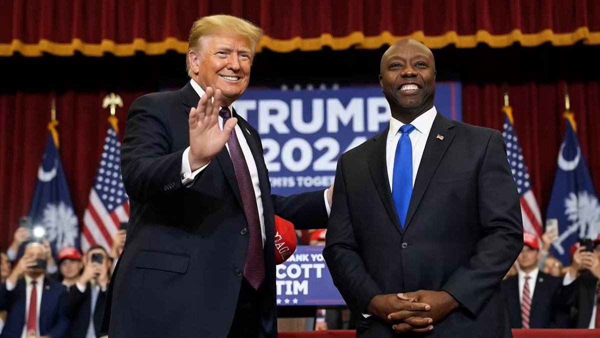 The image shows two men standing side by side, both wearing suits and ties, with one man waving at the camera while the other man has his hands together. The background features a stage setting with a podium and flags, suggesting that they are attending an event or gathering related to cryptocurrency regulation. A banner in the background displays "THE TRUMP presidency 2020", indicating that this is likely taking place during the 2020 presidential campaign season.